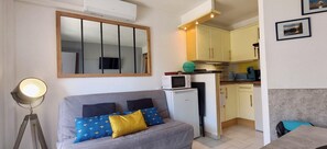 Un espacio habitable compacto con sofá, una kitchenette pequeña, microondas y aire acondicionado instalado en el techo.