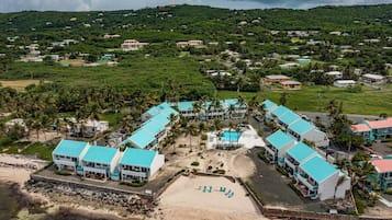 Ein Resort mit mehreren Gebäuden, einem Strand und hügeliger Landschaft im Hintergrund.