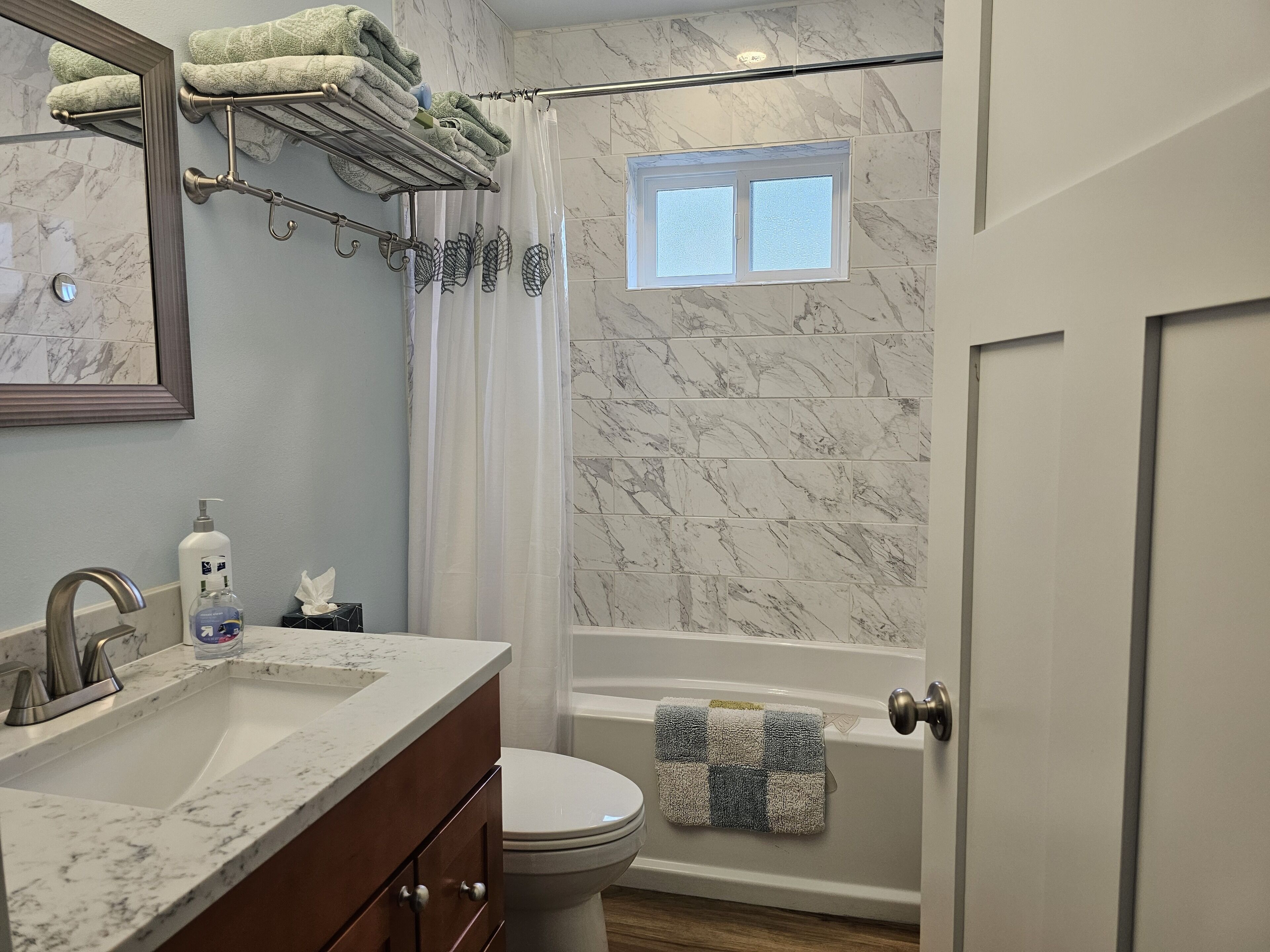 A bathroom with a marble-tiled shower, a toilet, a sink with a marble countertop, and a towel rack with folded towels.