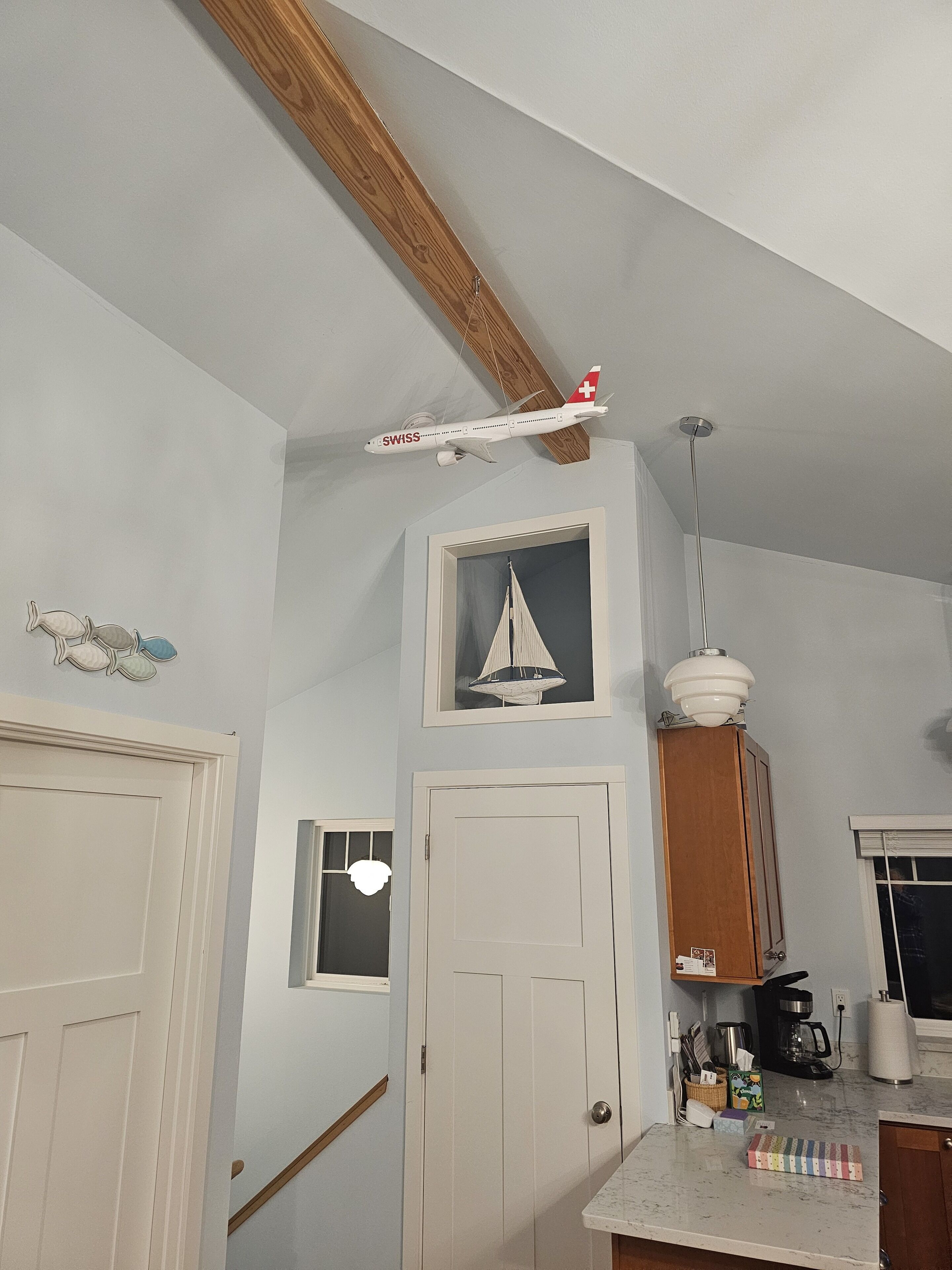 A kitchen with a wooden ceiling beam, a framed sailboat picture, and a Swiss airplane model.