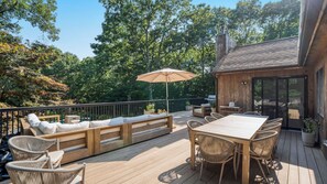 A wooden deck with outdoor furniture, including a table and chairs, and a bench with cushions. - Newly Renovated, Serene Property with Heated Pool, Tennis, and Resort-Like Spa (Southampton)