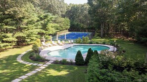 A backyard with a swimming pool, a tennis court, and a paved walkway. - Newly Renovated, Serene Property with Heated Pool, Tennis, and Resort-Like Spa (Southampton)
