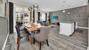 A modern kitchen with a central island, a dining area with a wooden table and chairs, and a living area with a sofa and TV. - Modern 4 Bed Townhome with Private Pool-9073DLD (Davenport)