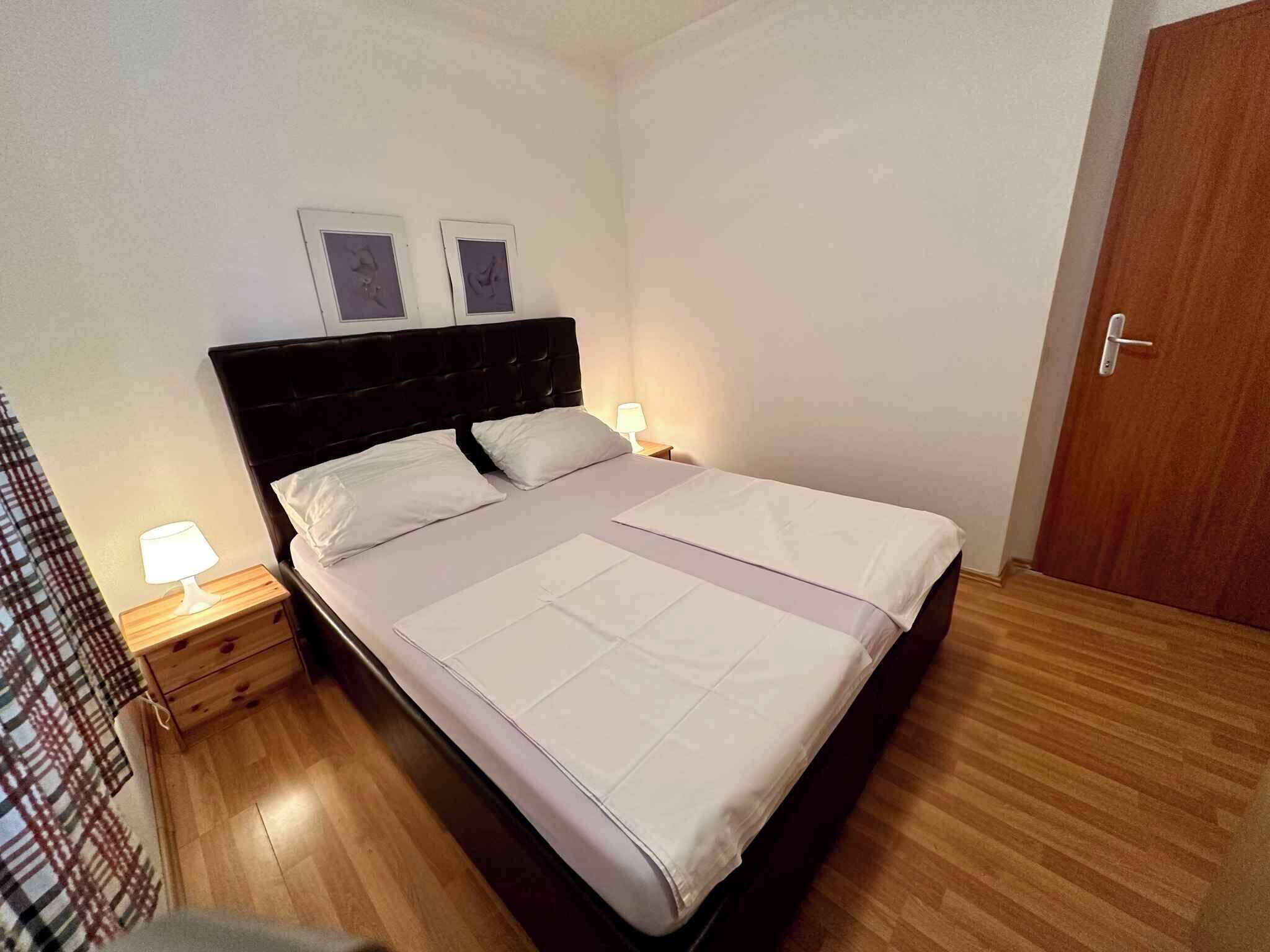 Una cama bien hecha con cabecera, dos lámparas de noche y suelo de madera.