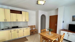 A compact kitchen with yellow cabinets, a dining table with chairs, and a television on a cabinet. - Holiday apartment with Wi-Fi (Novi Vinodolski)