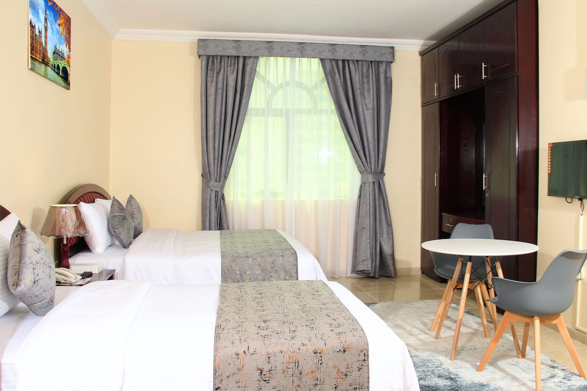 A hotel room with a bed, bedside table, lamp, curtains, a TV, and a small round table with chairs.