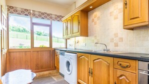 Cocina compacta con armarios de madera, lavadora y vistas al exterior.