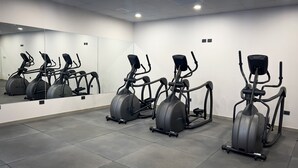 Een sportschool met meerdere elliptische trainers, een grote spiegel en een betegelde vloer.