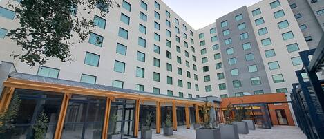 Un hotel moderno con un espacio exterior cubierto, amplias ventanas y un patio con jardineras.
