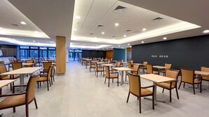Een ruime eethoek met meerdere tafels en stoelen, grote ramen en een modern plafondontwerp.