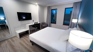 Een hotelkamer met een bed, een bureau, een stoel, een televisie en een raam met gordijnen.