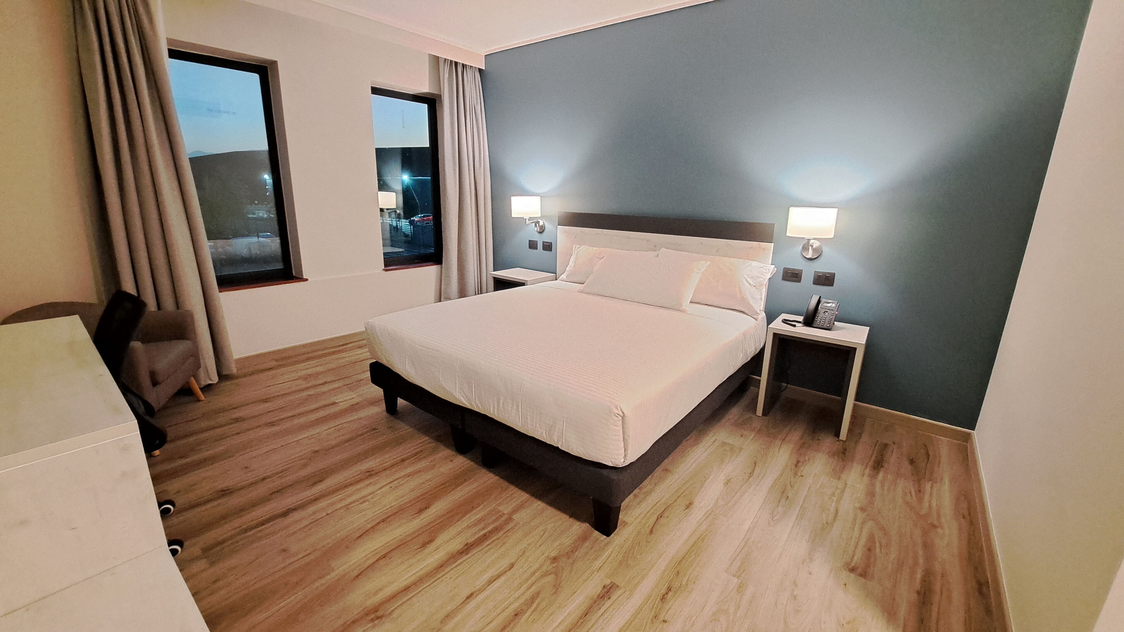 A hotel room with a bed, bedside lamps, a desk, and a chair.