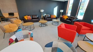 Een moderne lounge met leren banken, ronde tafels en kleurrijke stoelen.