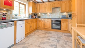 A kitchen with wooden cabinets, a dishwasher, an oven, and a window. - Owl Barn (Hereford)