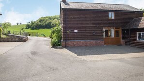 A rustic wooden building with a brick foundation, a wooden door, and a small window. - Owl Barn (Hereford)