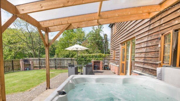 A hot tub under a wooden pergola with a wooden house in the background. - Owl Barn (Hereford)