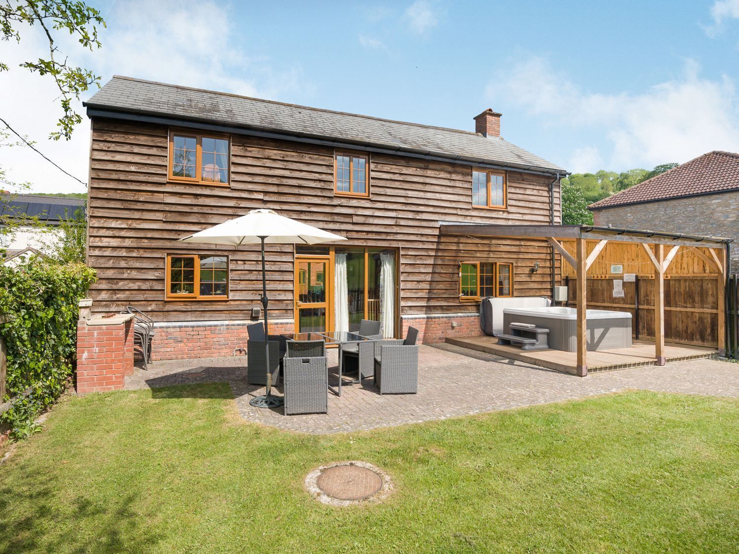 A two-story wooden house with a patio area featuring outdoor seating and a hot tub.