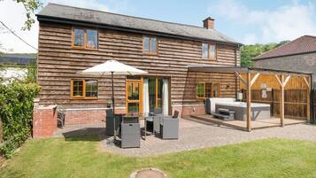 A two-story wooden house with a patio area featuring outdoor seating and a hot tub.