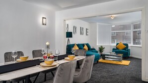 Ein modernes Wohnzimmer mit einem türkisfarbenen Sofa, einem Essbereich mit einem langen Tisch und einem Schild mit der Aufschrift 'HOME'.