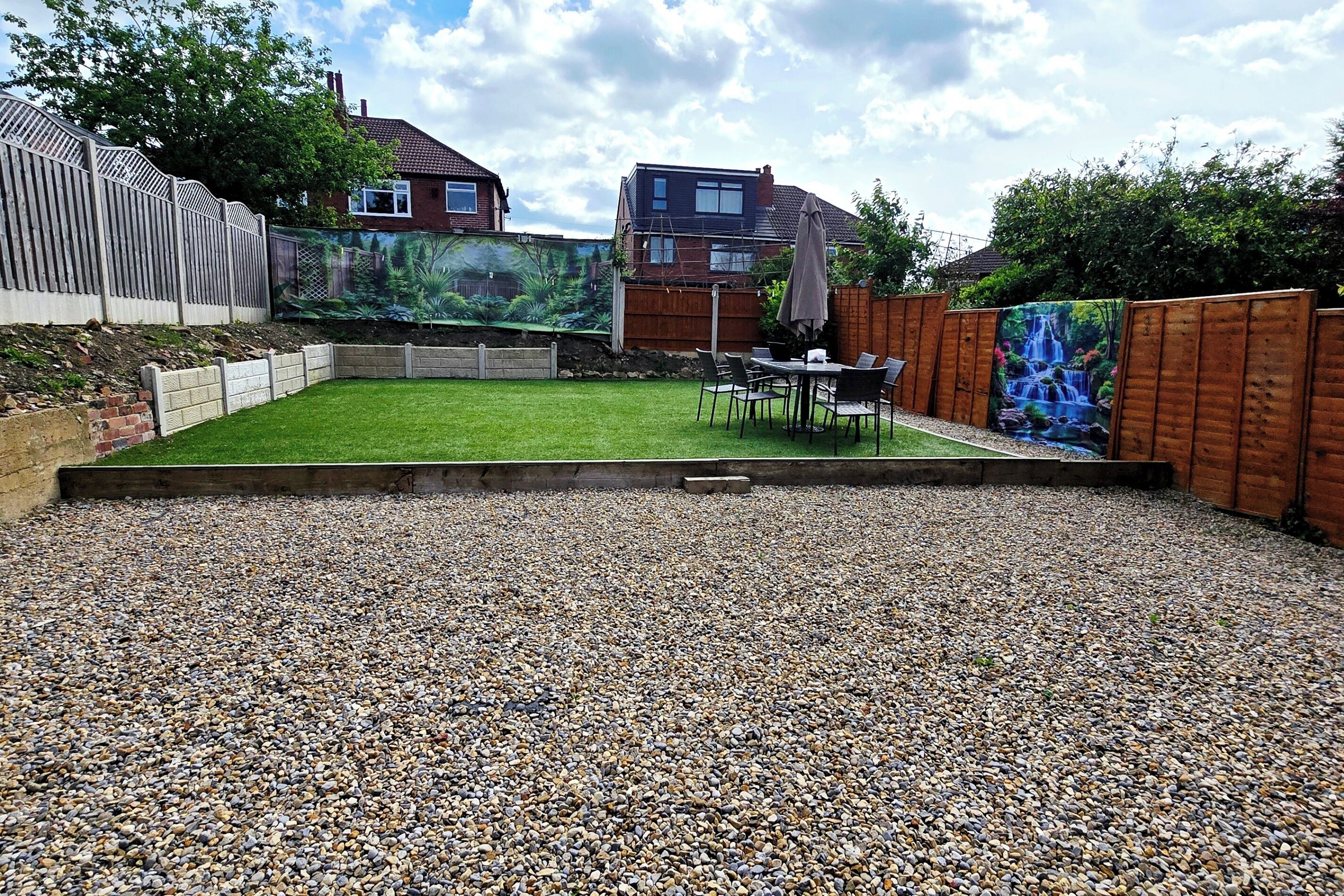 A backyard with a lawn, a gravel area, a wooden fence, and a mural.