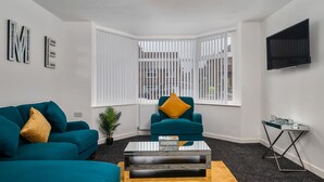 Ein modernes Wohnzimmer mit türkisfarbenen Sofas, einem Glastisch und einem an der Wand befestigten Fernseher.