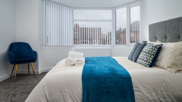 Ein Hotelzimmer mit einem großen Bett, einem blauen Sessel, einer Heizung und einem Fenster mit Jalousien.