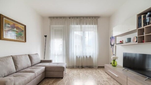 Uma sala de estar moderna com um sofá seccional bege, uma televisão de tela plana e uma estante.