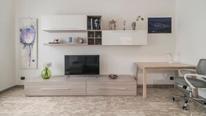 Uma sala de estar moderna com televisão de tela plana, escrivaninha de madeira e uma poltrona confortável.