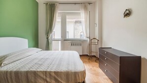 Quarto com cama, cómoda, radiador e janela com cortinas.