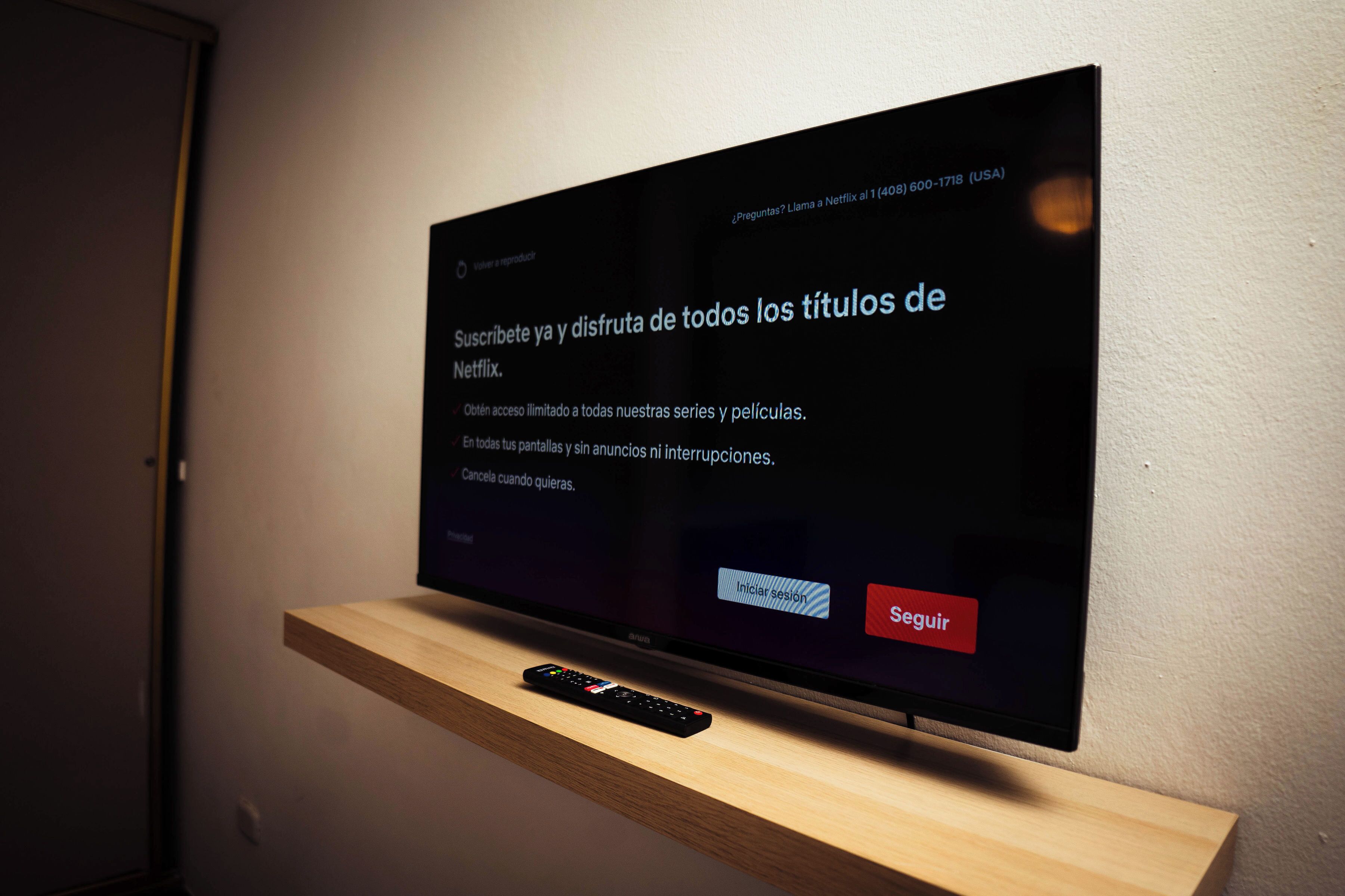 A flat-screen TV mounted on a wooden shelf with a remote control beside it.