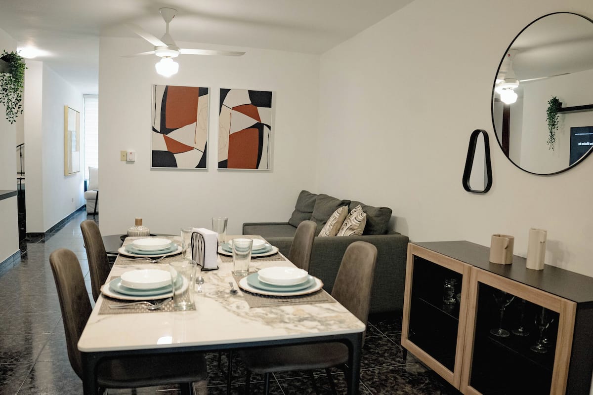 A dining area with a table set for four, a sofa, and a cabinet with wine glasses.