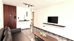 A modern living room with a sofa, a coffee table, a TV, and a ceiling fan. - Residenciales H1 & H2 (Santiago de los Caballeros)