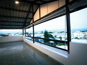 A spacious balcony with large windows overlooking a cityscape and mountains.
