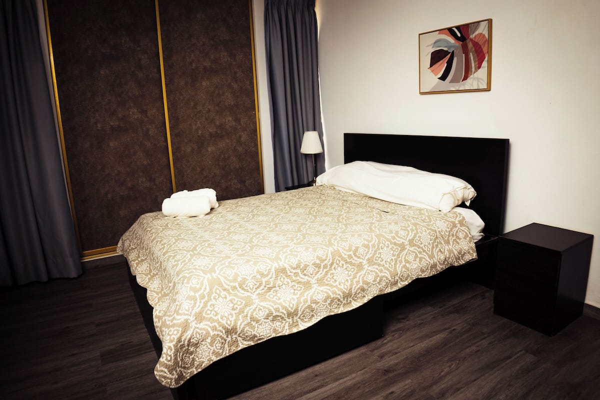 A neatly made bed with a patterned bedspread, a bedside table, and a wall-mounted lamp.