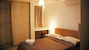 Habitació d'hotel amb un llit, una taula de nit amb una làmpada, un armari i un ventilador de sostre.