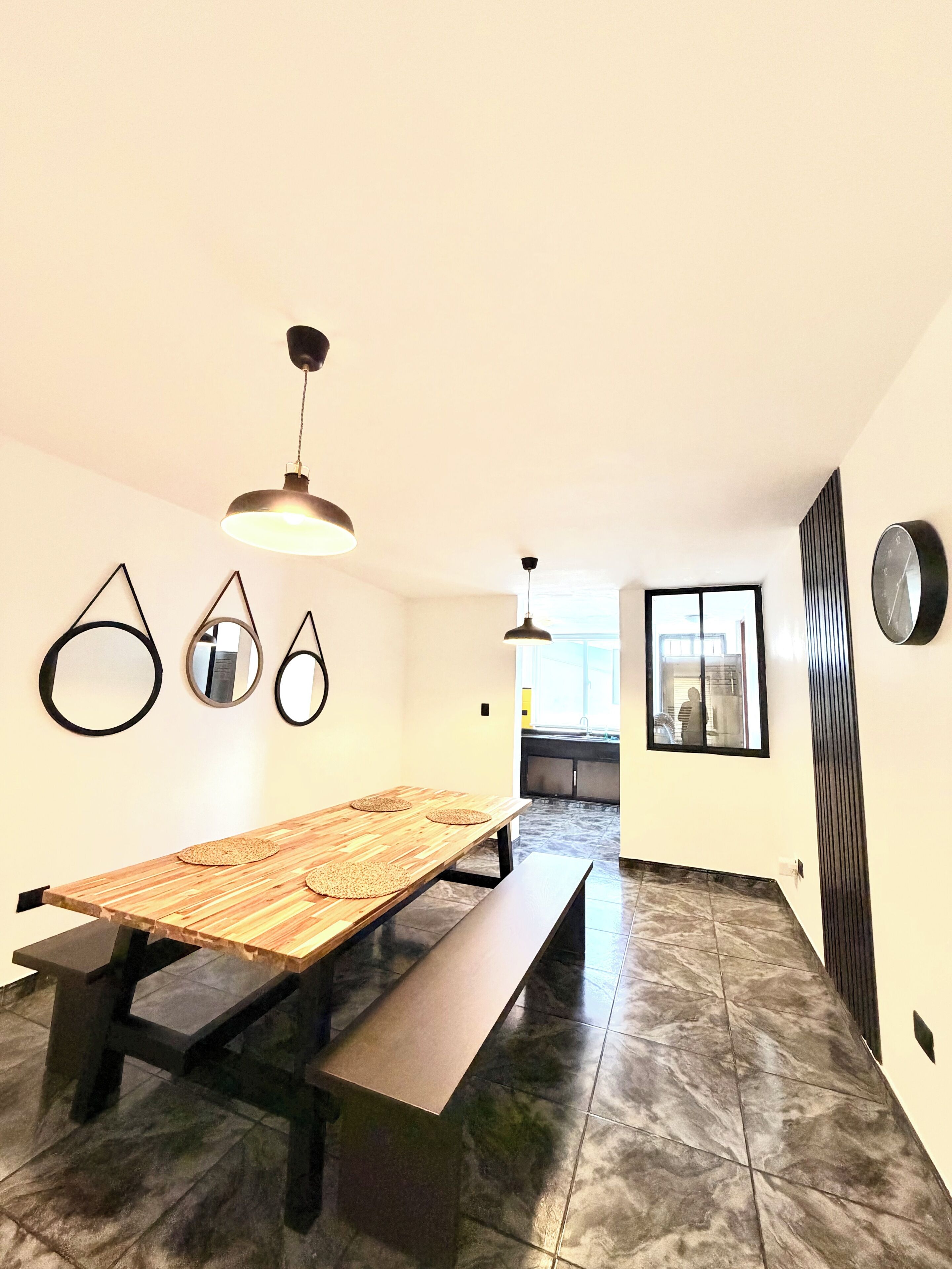 Una cocina moderna con una isla grande, un comedor con mesa y banco de madera, y vistas al exterior a través de una ventana.
