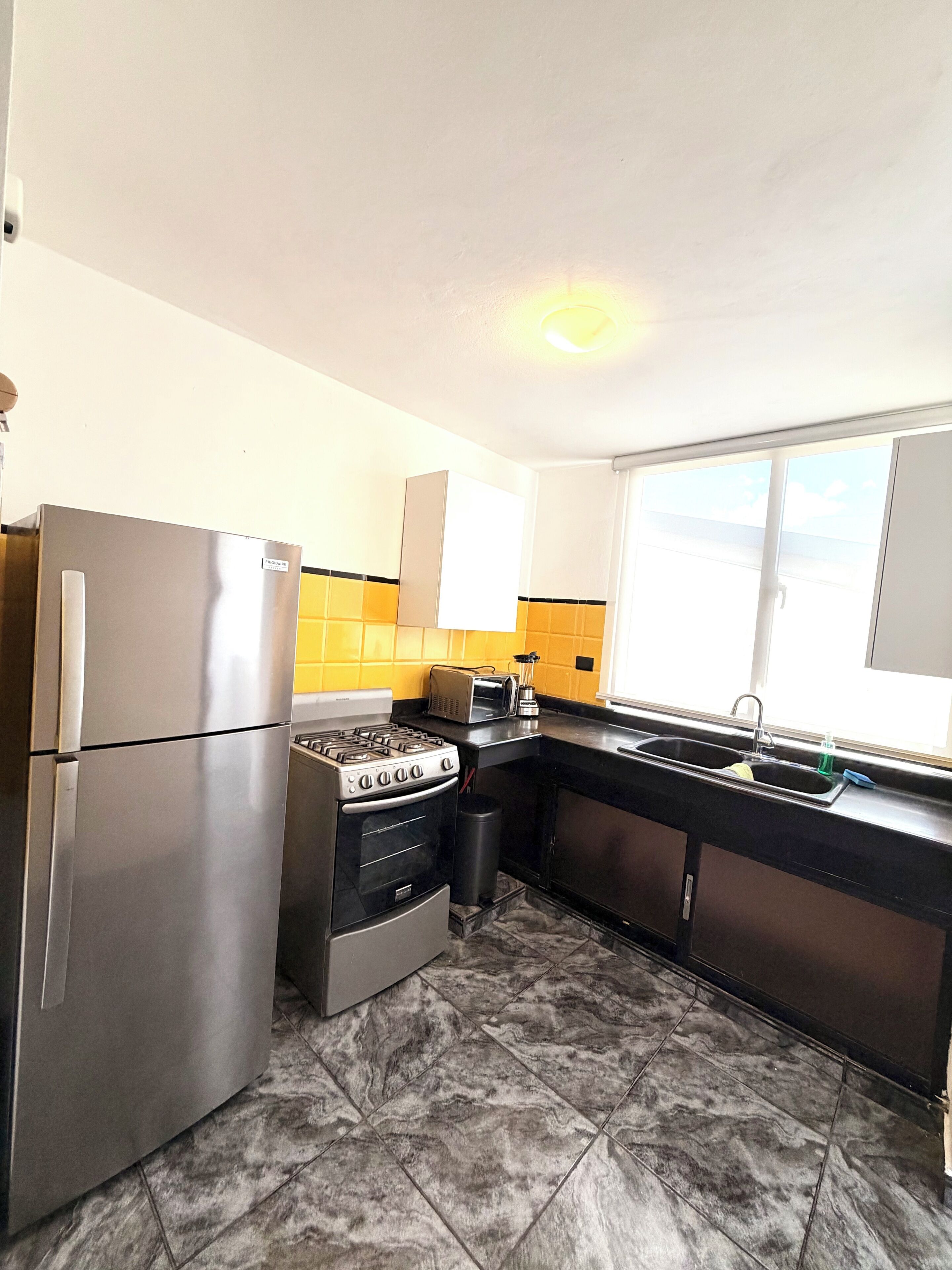 A kitchen with a stainless steel refrigerator, a gas stove, a sink, and a window with a view.