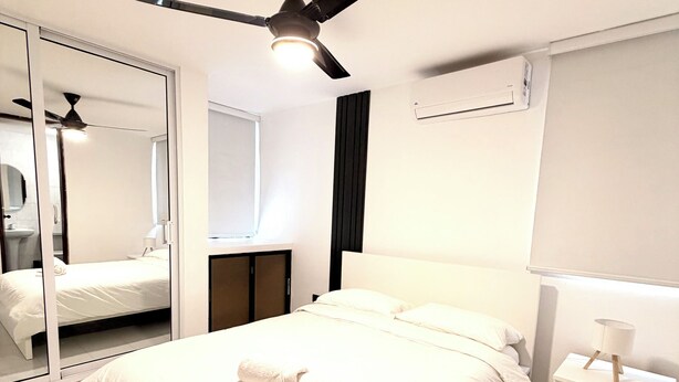 A modern hotel room with a large bed, a ceiling fan, a bedside table with a lamp, and a mirror. - Residenciales H1 & H2 (Santiago de los Caballeros)