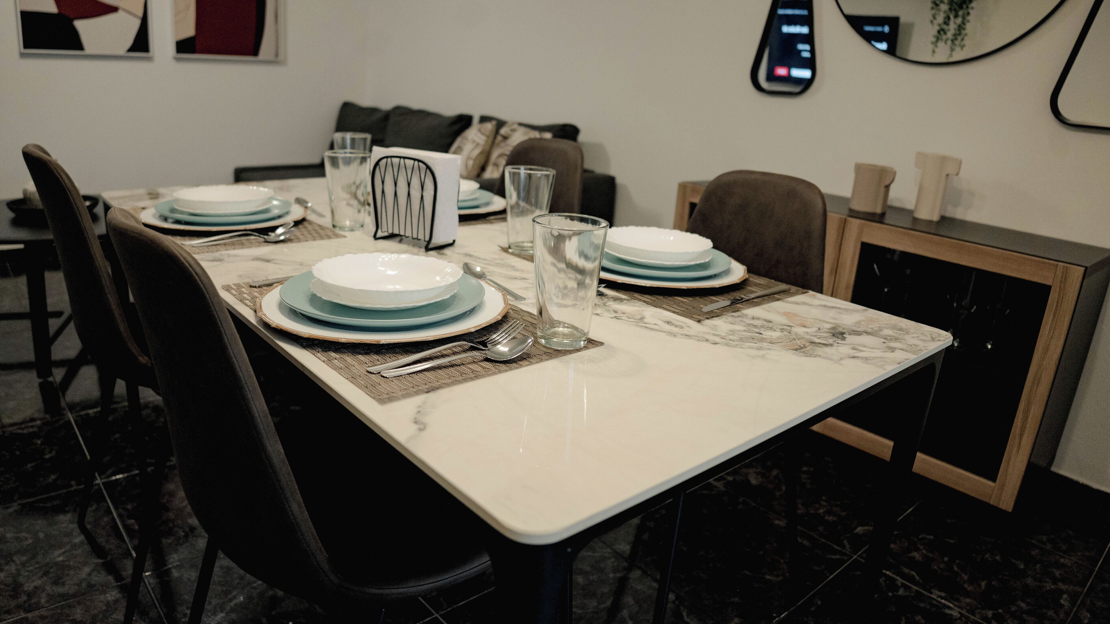 A dining table set with plates, glasses, and cutlery, surrounded by chairs.