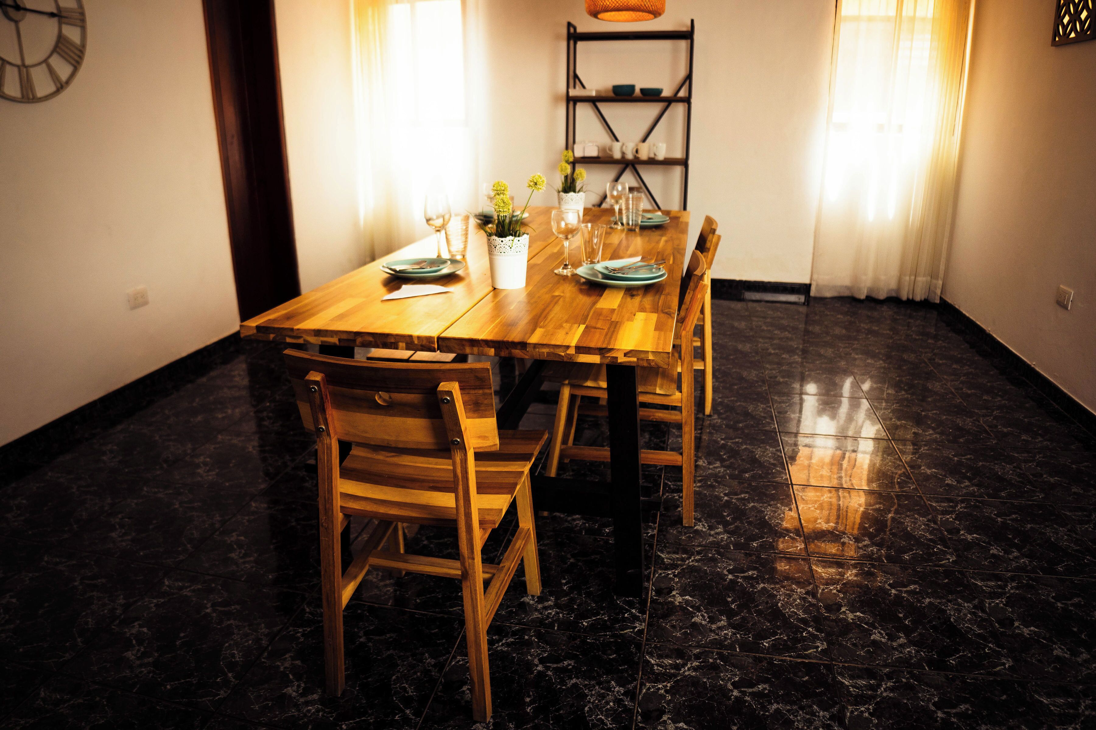 A dining area with a wooden table and chairs, a shelf with dishes, and a clock on the wall.