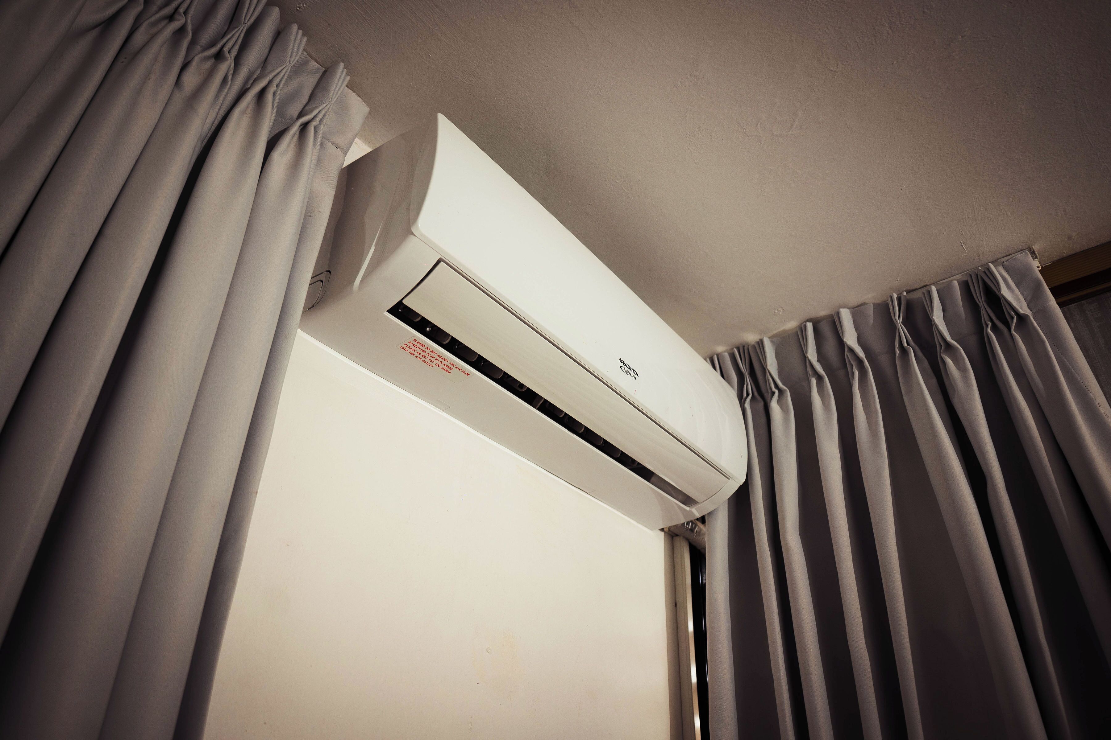 Un appareil de climatisation blanc, fixé au mur dans une pièce où sont accrochés des rideaux gris.