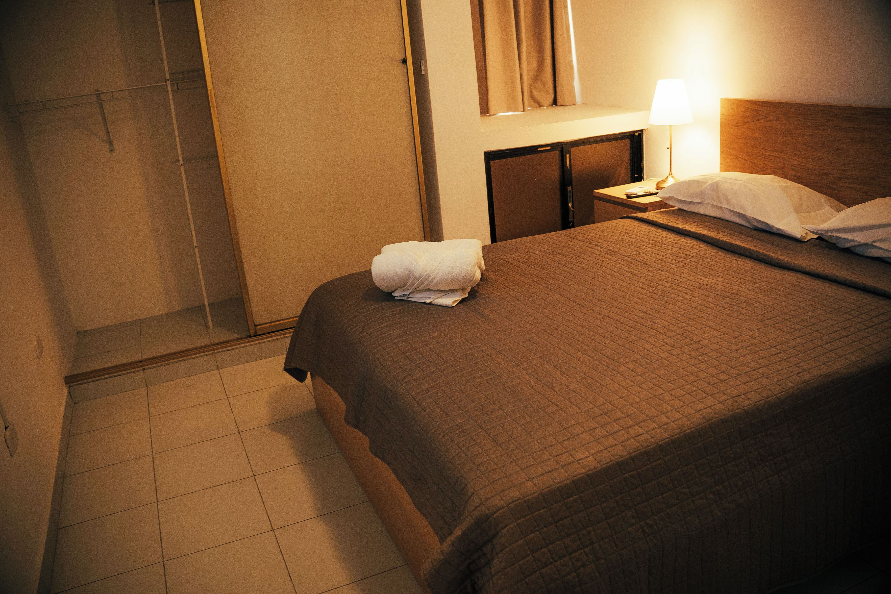 Een hotelkamer met een bed, nachtkastje, lamp, handdoek en kast.