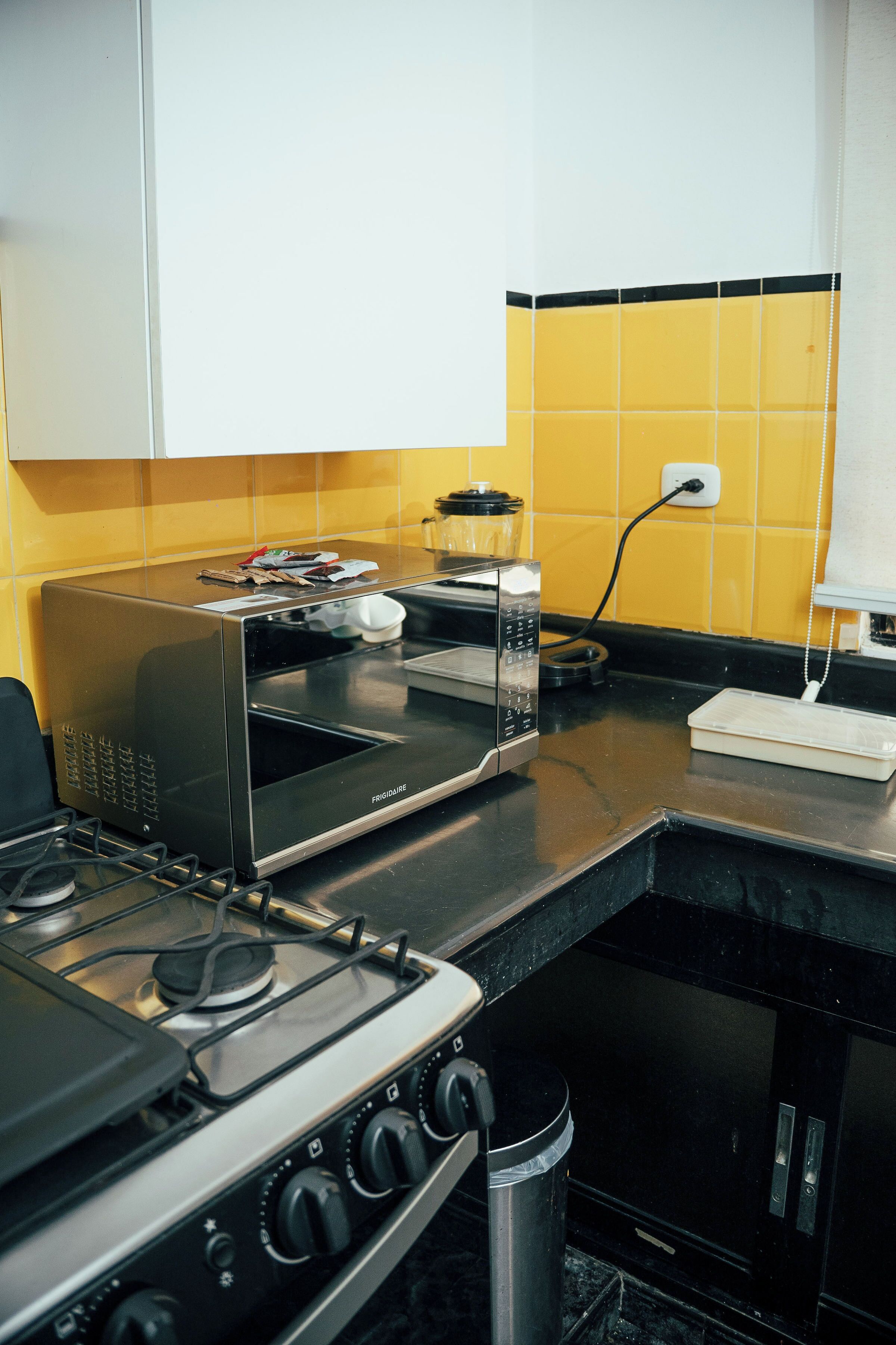 A kitchen with a stove, microwave, and yellow-tiled backsplash.