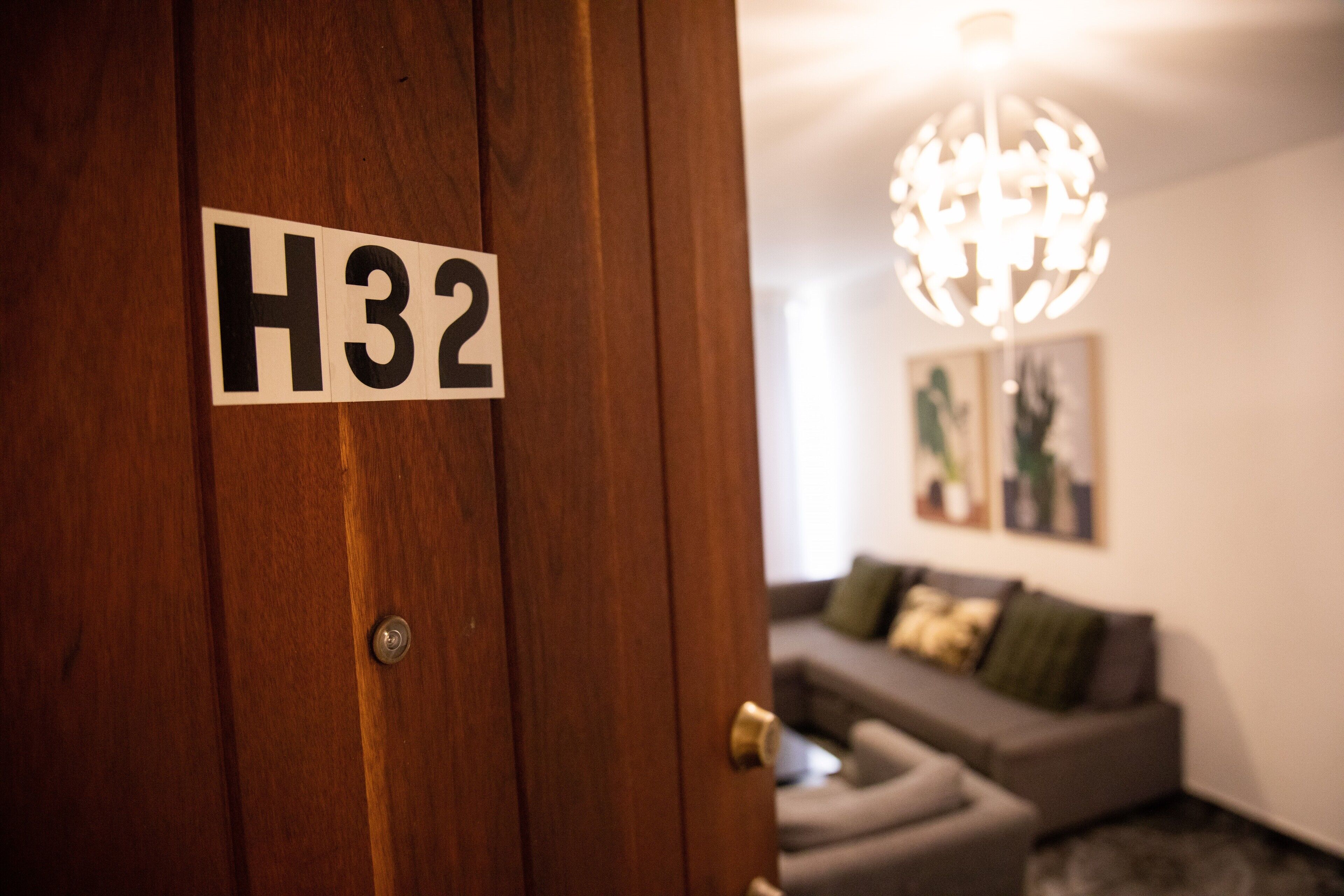 Une porte en bois sur laquelle est apposée une plaque portant l’inscription « H32 », et un lustre moderne en arrière-plan.
