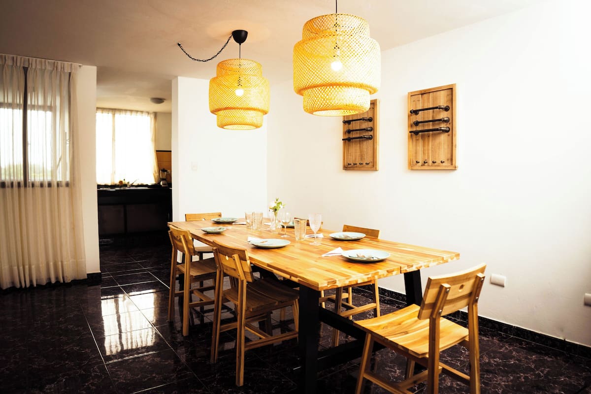 A dining area with a wooden table and chairs, a chandelier, and a wooden cabinet on the wall.