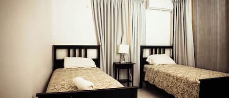 Habitación de hotel con dos camas individuales, ventilador de techo, equipo de aire acondicionado y ventana con cortinas.