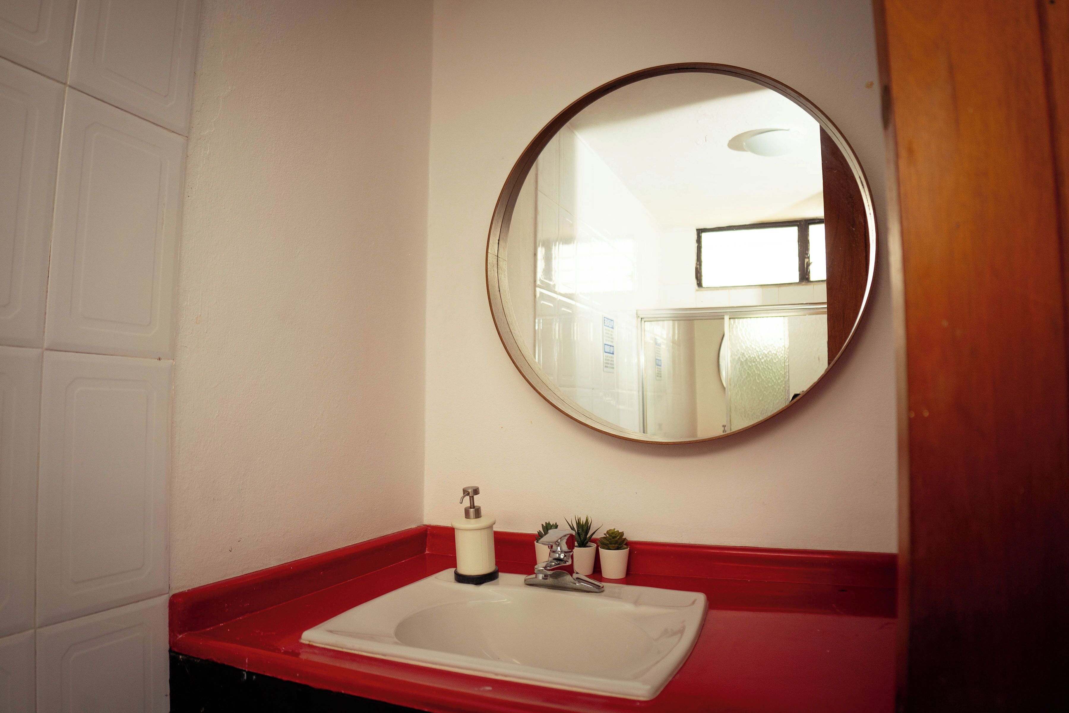 A bathroom with a white sink, red countertop, and a round mirror.