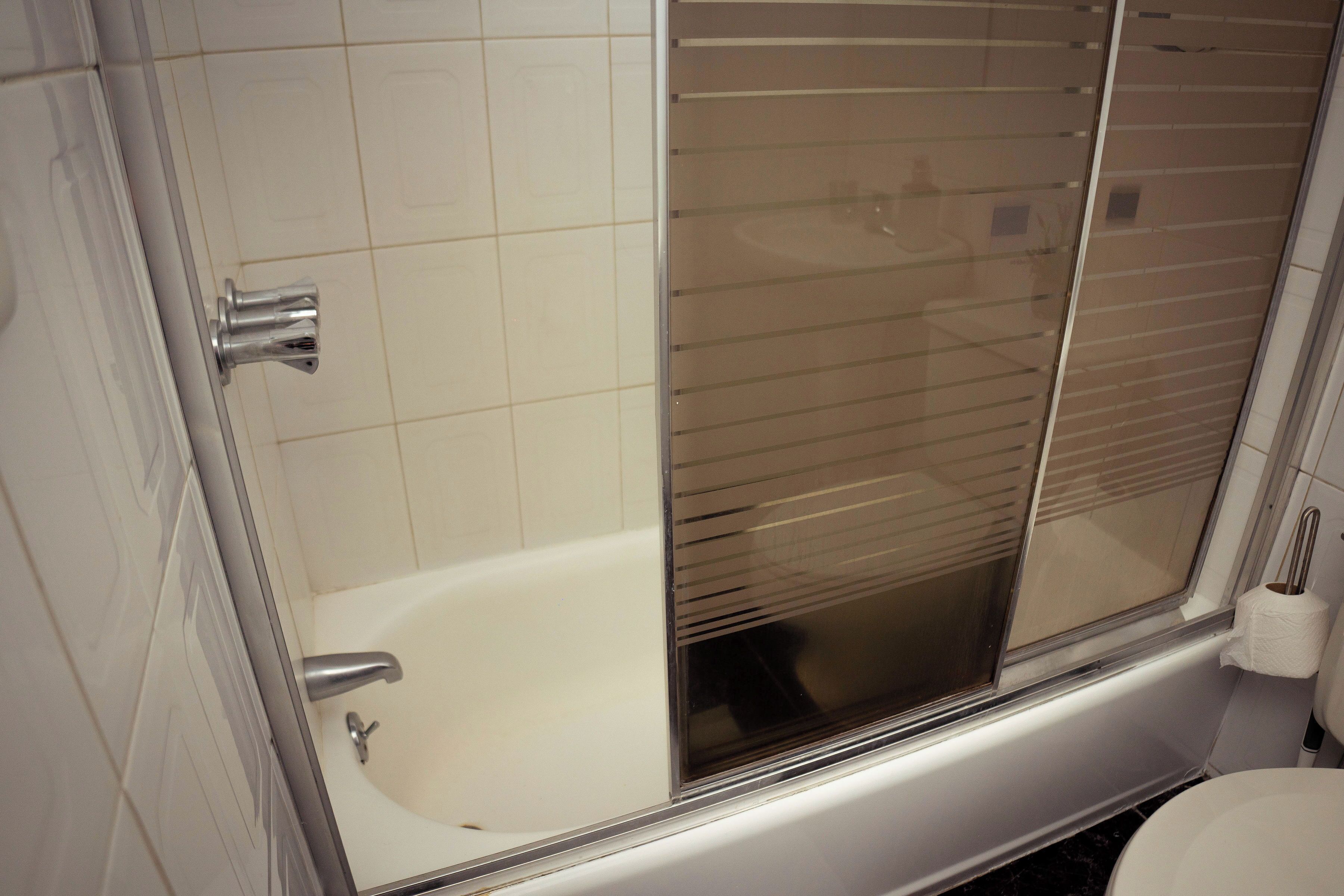A bathroom with a bathtub, toilet, and a window with blinds.