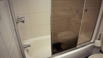 A bathroom with a bathtub, toilet, and a window with blinds.