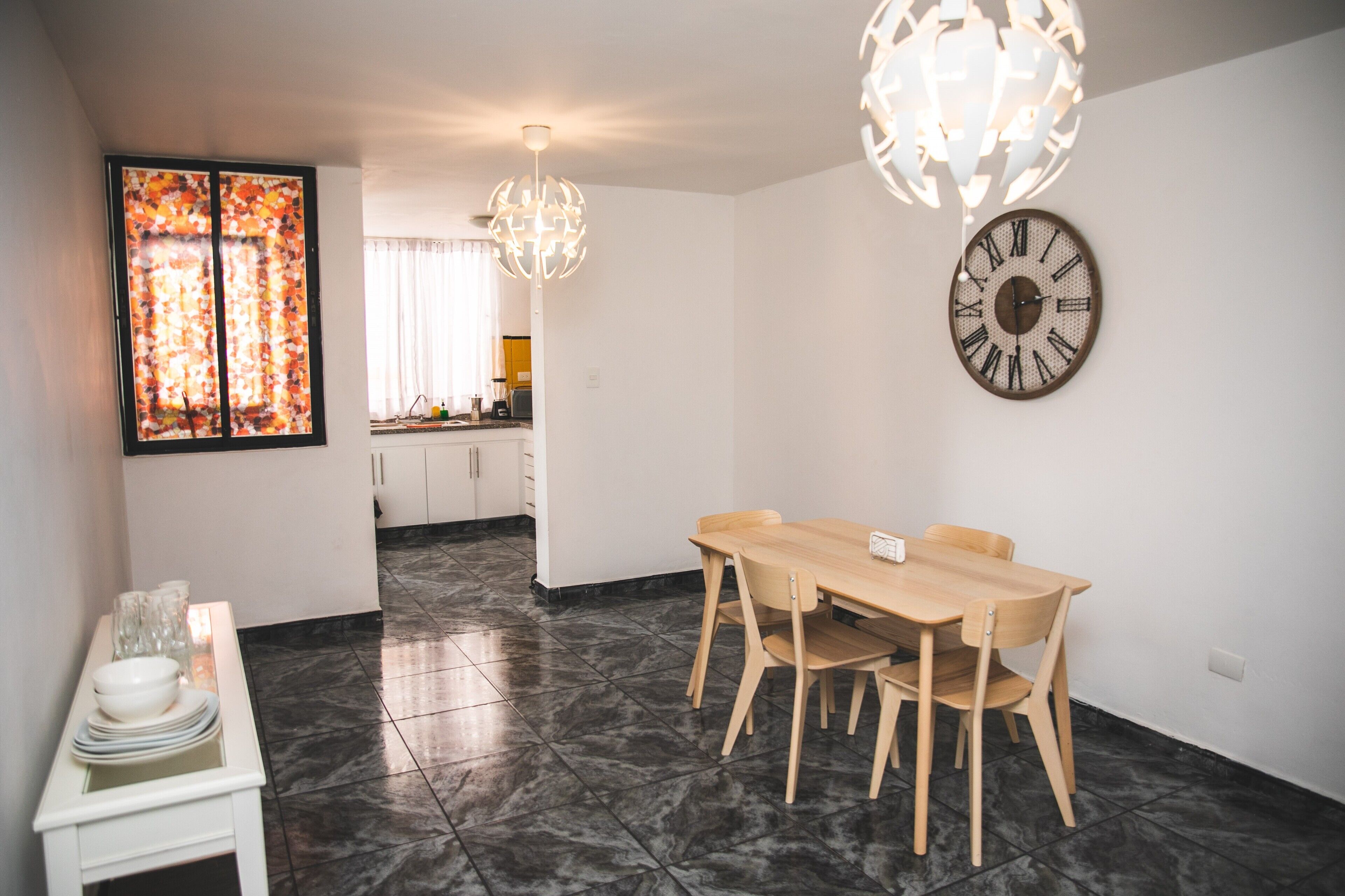 A dining area with a wooden table and chairs, a decorative wall clock, and a modern chandelier.